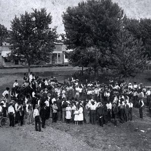 Large group of people on town square with buildings and trees in background