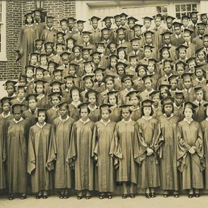 Group of African American students in graduation caps and gowns on steps of brick building