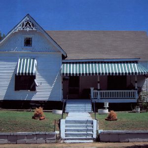 Front view of house with white siding and covered porch with green and white striped awning