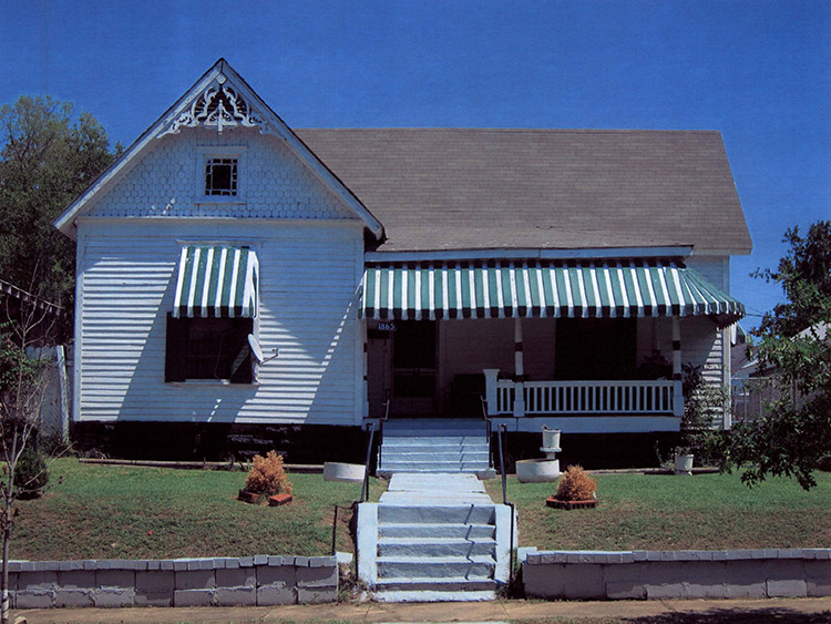 Front view of house with white siding and covered porch with green and white striped awning