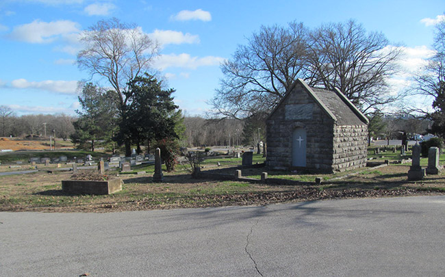 Brick mausoleum in cemetery with paved road in the foreground