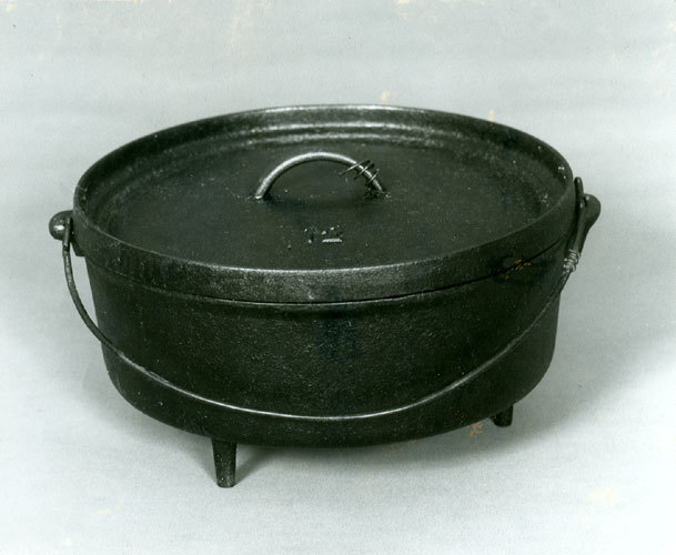 Large black Dutch oven of cast iron with lid and handle on a white background