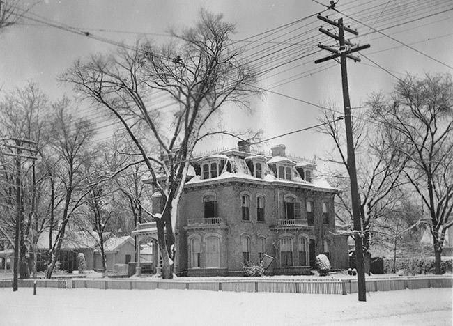 ornate multistory house inside fence with trees and snow covered yard