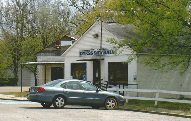Car parked in front of single-story building next to brick storefront with awning