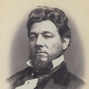 White man with curly hair and beard in suit