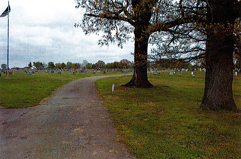 Narrow road in cemetery with tree and flagpole in the background