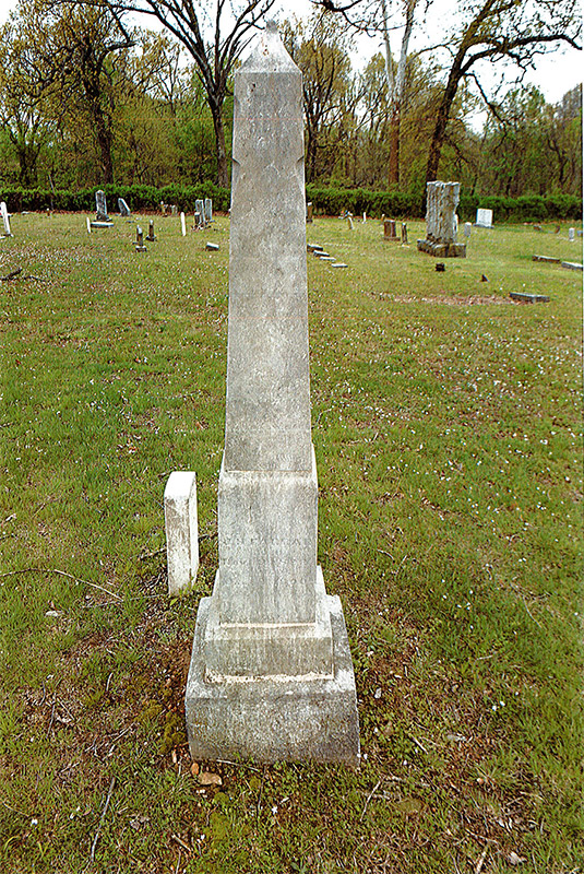 Obelisk shaped monument in cemetery with gravestones in the background