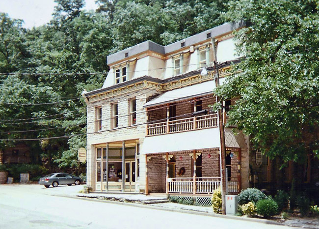 Three-story brick building with covered porch and balcony and parking lot with car