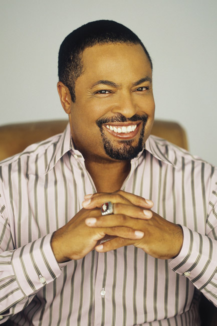 Portrait black man seated smiling goatee striped collared shirt fingers crossed with university ring