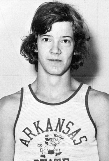 Young white man with curly hair in sleeveless "Arkansas" shirt featuring caricature of Native American