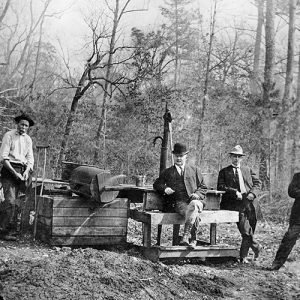 Group of white men in hats with mining equipment and bare trees behind