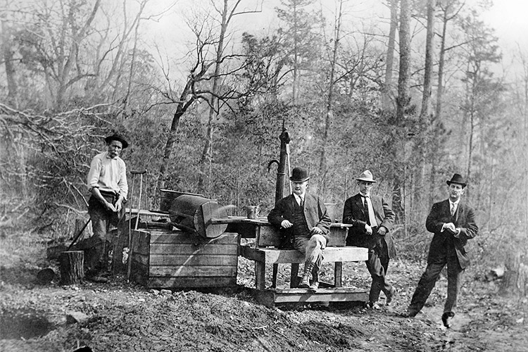 Group of white men in hats with mining equipment and bare trees behind