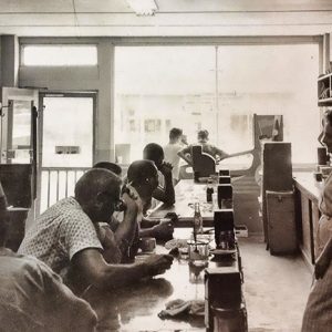 Men sitting at counter in restaurant with white woman behind the counter