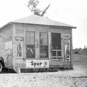 Small store with soda advertisements and car and gas pump on dirt road