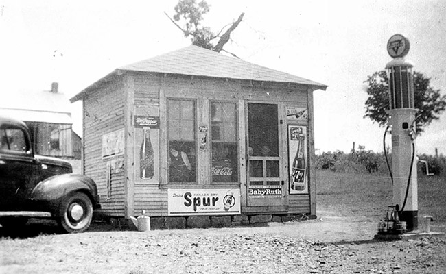 Small store with soda advertisements and car and gas pump on dirt road