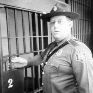 White policeman in uniform with wide brimmed hat standing at jail cell door
