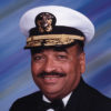 African-American man with mustache smiling in tuxedo with badges and naval cap