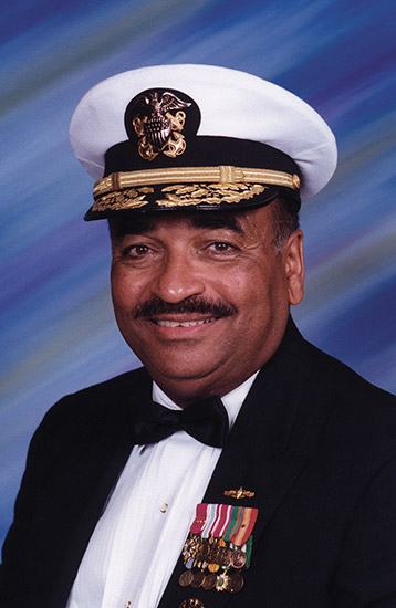 African-American man with mustache smiling in tuxedo with badges and naval cap