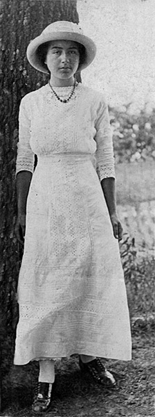 Young white woman in hat and dress standing next to a tree
