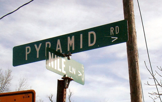Street signs for "Pyramid Road" and "Nile Lane" with telephone pole and blue skies