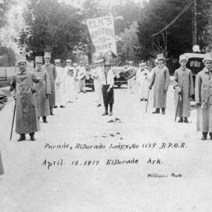 white men in top hats and long coats posed on either side of man holding sign that reads "Elk's Minstrel Tonight."