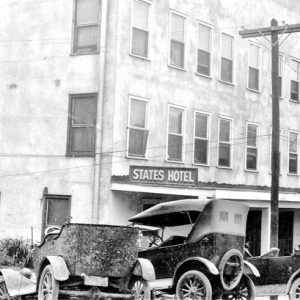 Three-story hotel "States Hotel" with parked cars and power lines and cars in front