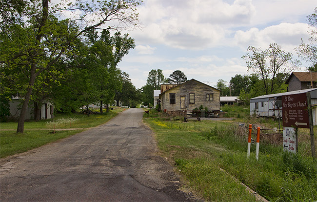 road with signs and mobile home and run-down houses on right side
