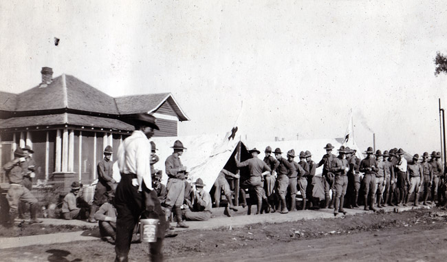 White soldiers in uniforms at camp with house and row of tents