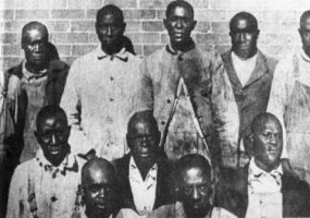 Group of African-American men standing and sitting before brick wall