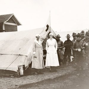 White soldiers with cups and two white women in nurses uniforms standing outside white tents