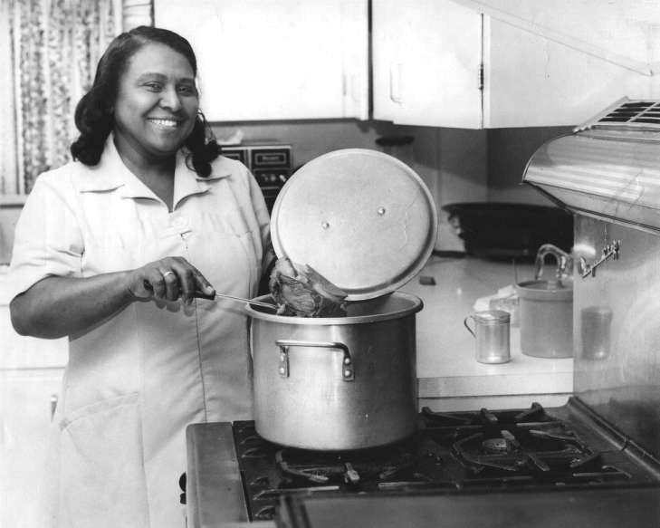 African-American woman cooking in kitchen with pot on stove