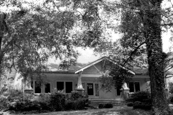 Front view of house with covered porch under large tree on street