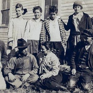 Group of white children sitting and standing outside building with wood siding