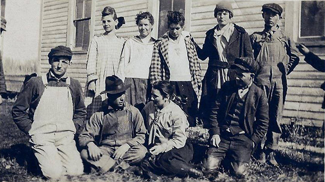 Group of white children sitting and standing outside building with wood siding