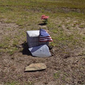 Broken gravestone with small American flag in cemetery