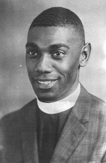 Young African-American man with close-cropped hair in suit with white clerical collar