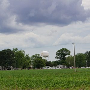 Green field with water tower and buildings in the distance