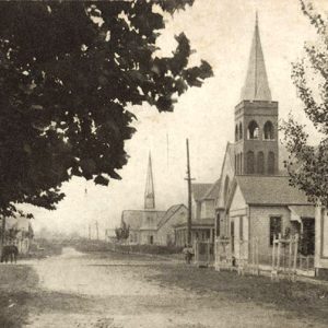 Two church buildings with bell towers and houses on town street with other buildings