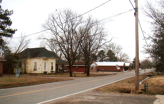 House and brick buildings on street with trees and power lines