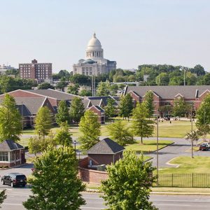 Campus with multistory brick buildings and parking lots with multistory buildings and capitol building in the background