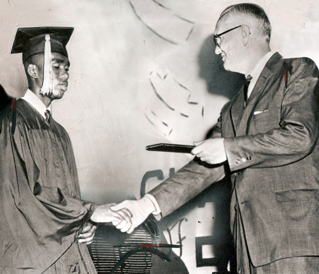 White man in glasses and suit shaking hands with young African-American man in cap and gown