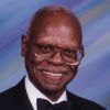 Older African-American man with glasses and mustache smiling in suit and bow tie