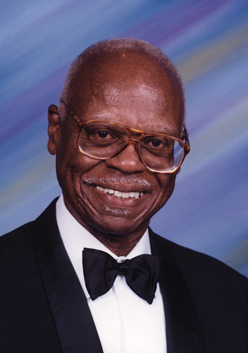 Older African-American man with glasses and mustache smiling in suit and bow tie