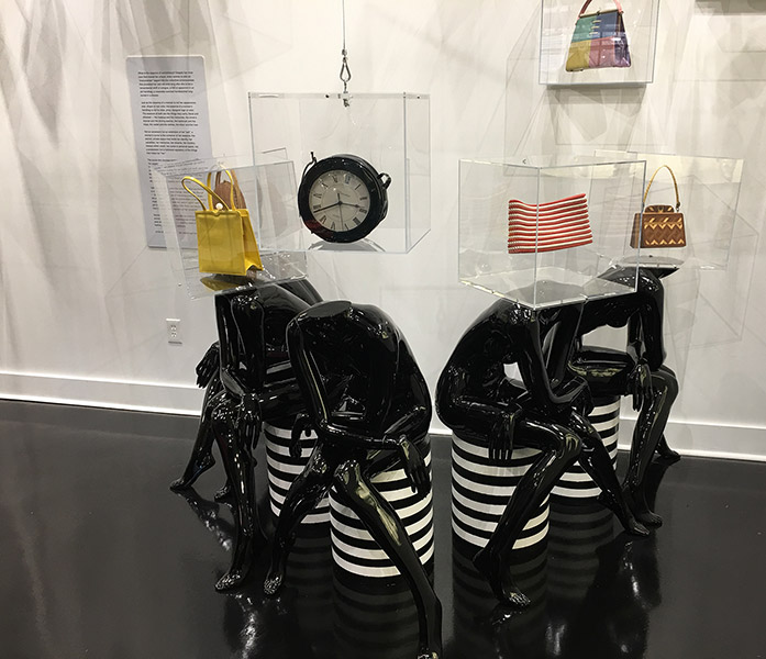 Headless mannequins with bags in display cases on top of them with clock in hanging case in museum