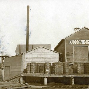 building with "Eudora Ginnery" sign with cotton bales smoke stack and water tower