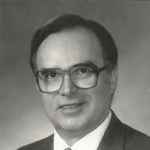White man with glasses smiling in suit and tie