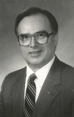White man with glasses smiling in suit and tie
