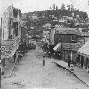 Looking down street with multistory storefronts on either side and houses on hillside in the backgrounds