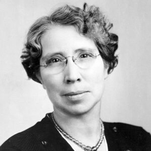 White woman wearing glasses and necklace over a black top with buttons