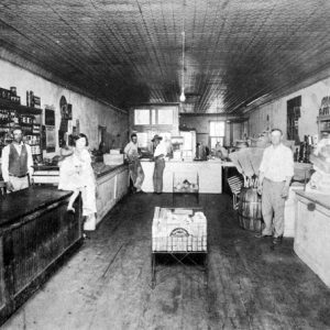 White men and women inside a general store with walls lined with goods and display counters